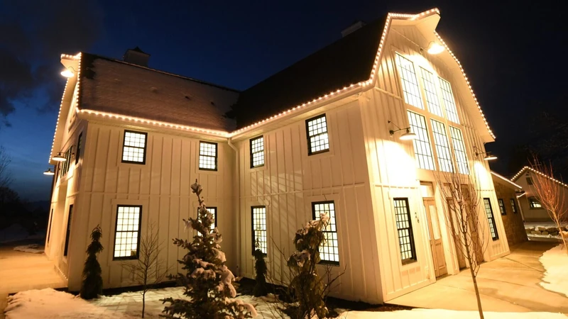 Warm white roofline Christmas lighting on a barn-style home in winter